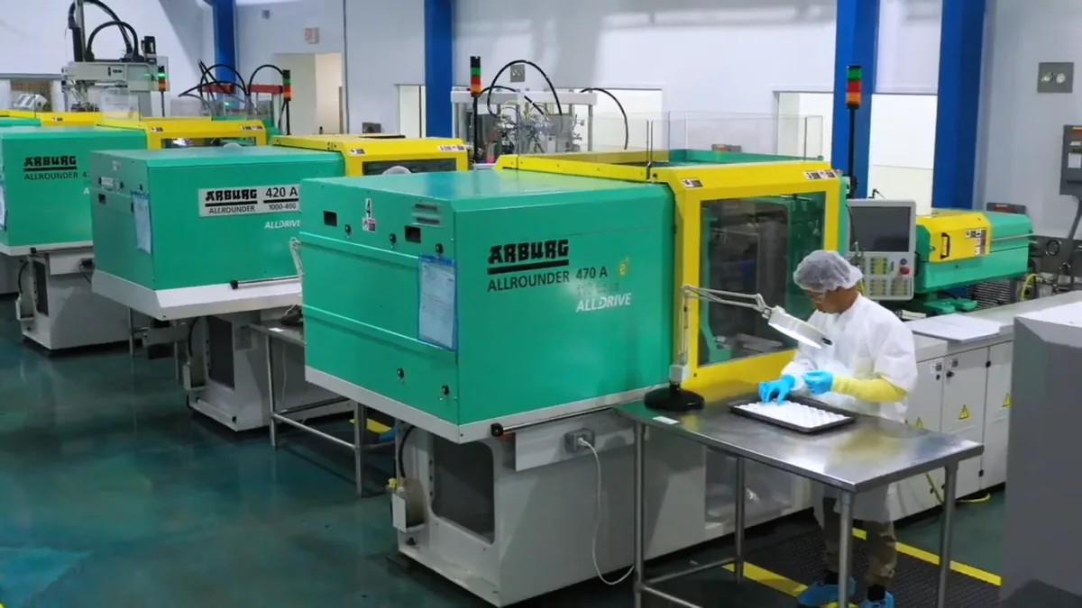 Liquid silicone molding presses on the IRP Medical floor, with an operator inspecting a tray of parts