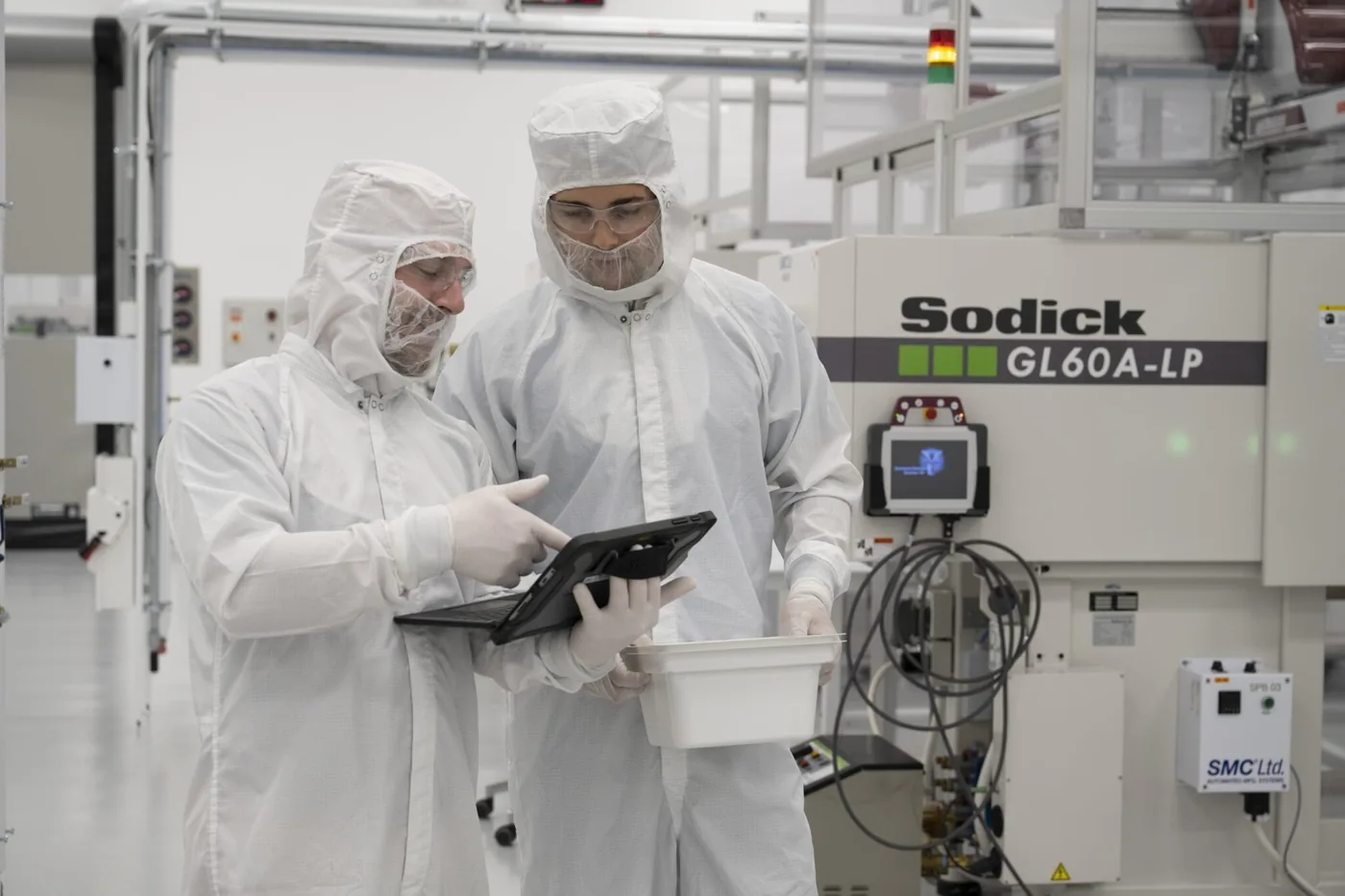 Two IRP Medical engineers in cleanroom gowns reviewing a tablet beside a molding press